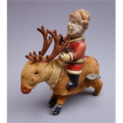  Early 20th century clockwork figure of Father Christmas with composition head and tin-plate body, riding a cloth covered reindeer with wheeled tin-plate front hoofs and integral winding key H15cm  
