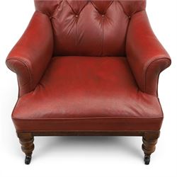 Early 20th century style oxblood red leather Chesterfield armchair, deep buttoned shaped back over padded scroll arms and loose seat cushion, raised on turned mahogany front supports with brass caps and castors