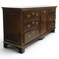 19th century Georgian oak long dresser base, rectangular plank top above a central frieze drawer over a fielded panel cupboard, flanked by three banks with quarter cantered pilasters, brass swan neck handles and escutcheons, raised on shaped bracket feet