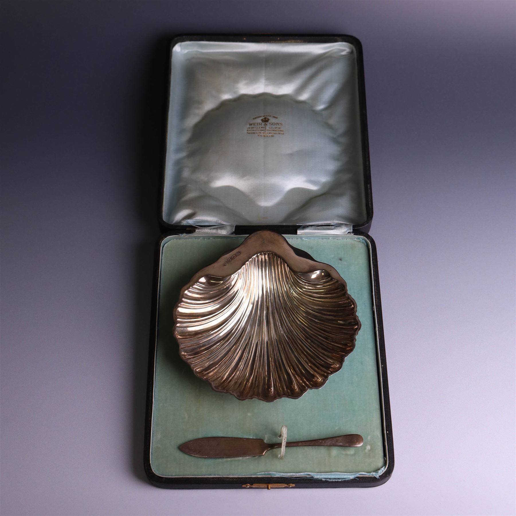 Edwardian silver butterdish in the form of a clam shell and upon four bun feet, hallmarked Williams Birmingham Ltd, Birmingham 1905, with a silver plated butter knife, contained within a fitted tooled leather case, width of dish 13cm
