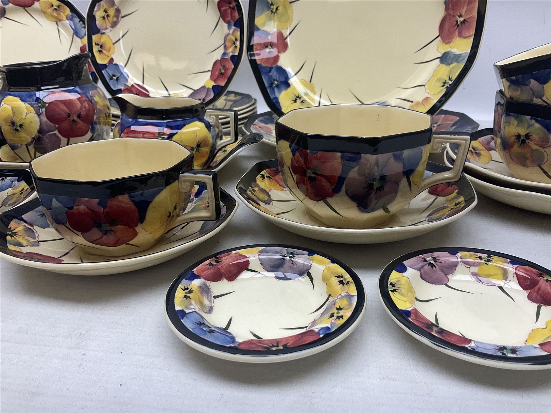 Early 20th century Art Deco Royal Doulton Pansies pattern octagonal teawares, comprising three larger teacups and saucers, three smaller teacups and saucers, open sucrier, two jugs, slop bowl, six side plates, two larger plates, two small circular dishes and one long twin handled rectangular dish, all with printed marks beneath, Rd No 597783, pattern no D4049