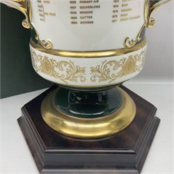 Aynsley twin handled racing cup and cover, to commemorate 'The Golden Jubilee of the Revival of The Yorkshire Cup', the handles inscribed '1927' and '1977', the green body painted by E. Woodhouse with Joe Childs up on Trimdon, the reverse with the winners, the domed cover with a Yorkshire rose finial, limited edition no. 4 of 50, on hexagonal wooden base with certificate, H34cm