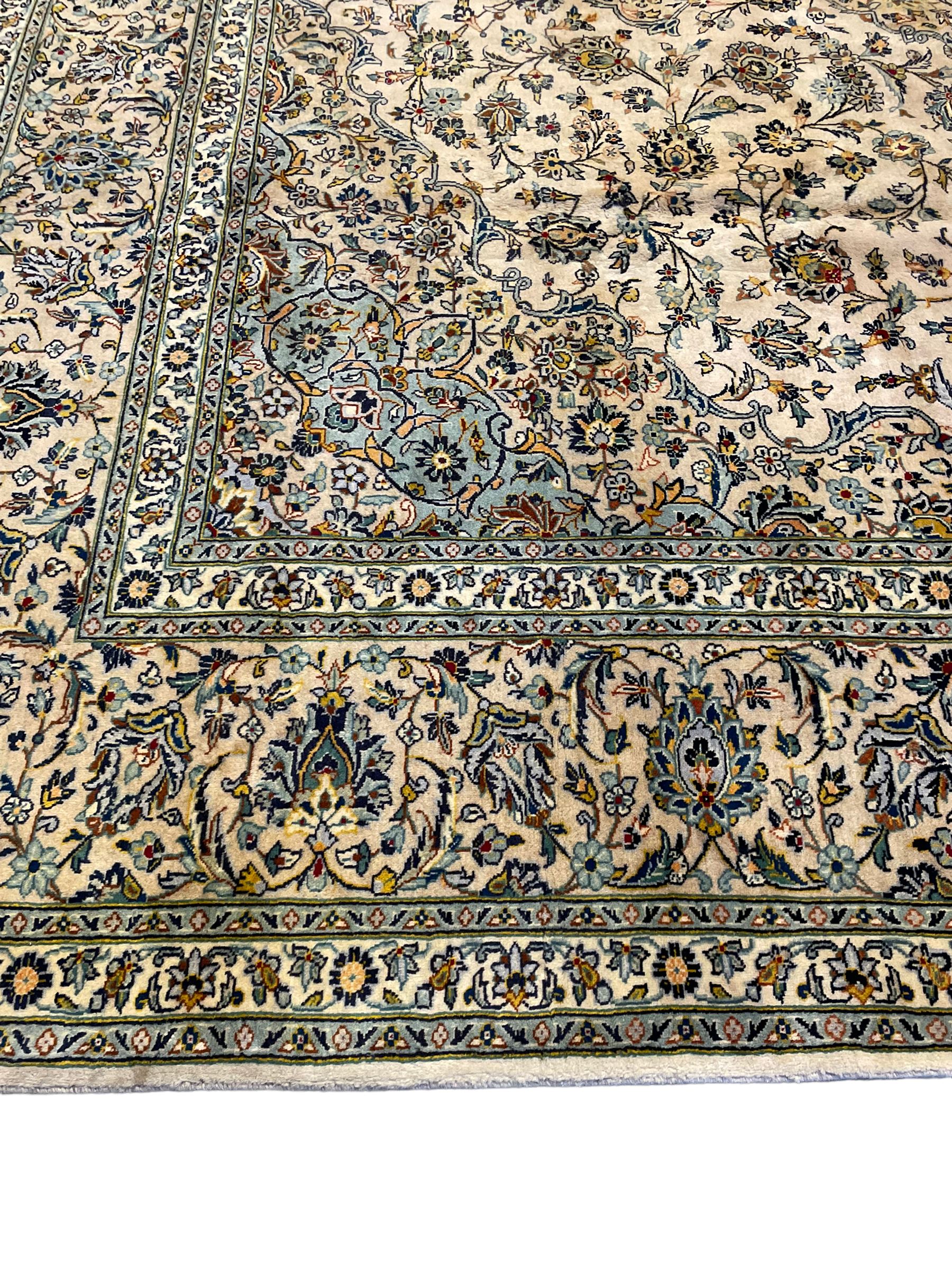 Central Persian Kashan pale khaki ground carpet, shaped central medallion enclosing small stylised motifs, the field decorated profusely with trailing foliate branches and plant motifs, guarded border with repeating floral design 