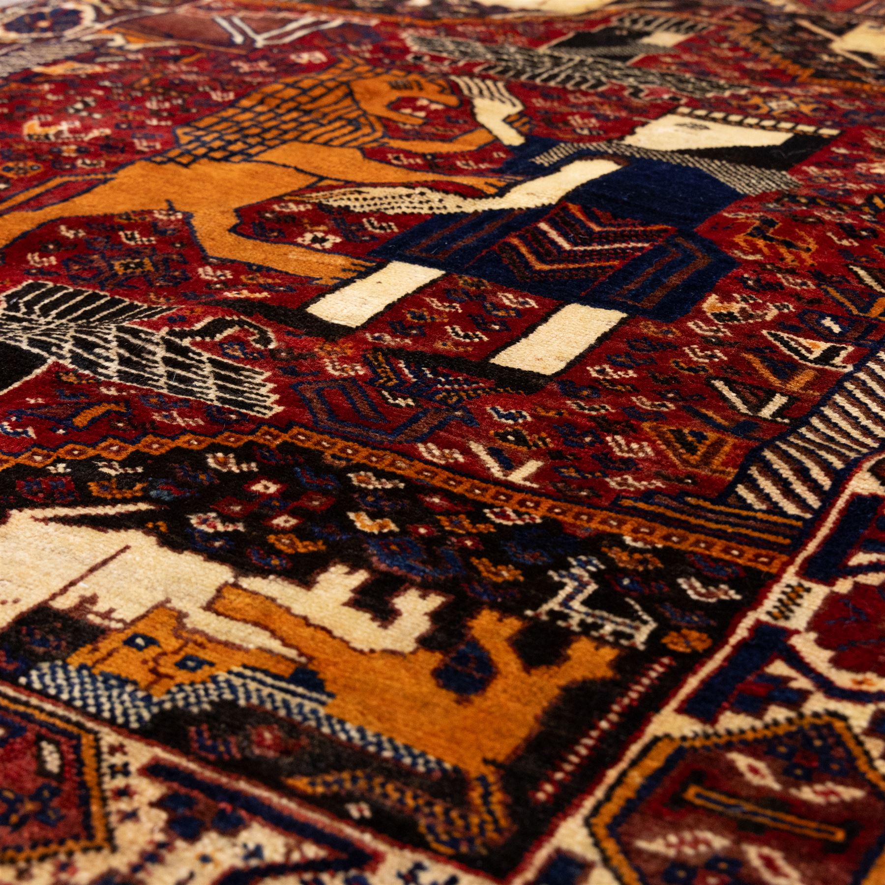 South West Persian Qahqai pictorial hand-knotted rug, madder red field with an all-over pattern of repeating rosettes enclosed with angular leaves and corners with stylized animals figures, central stylized lion in rearing stance and raised forelegs and a human figure shown in profile within a principal border of alternating octagonal and diamond medallions, each enclosing stylized rosettes, flanked by guard stripes incorporating latch hook motifs, with cotton fringe ends  