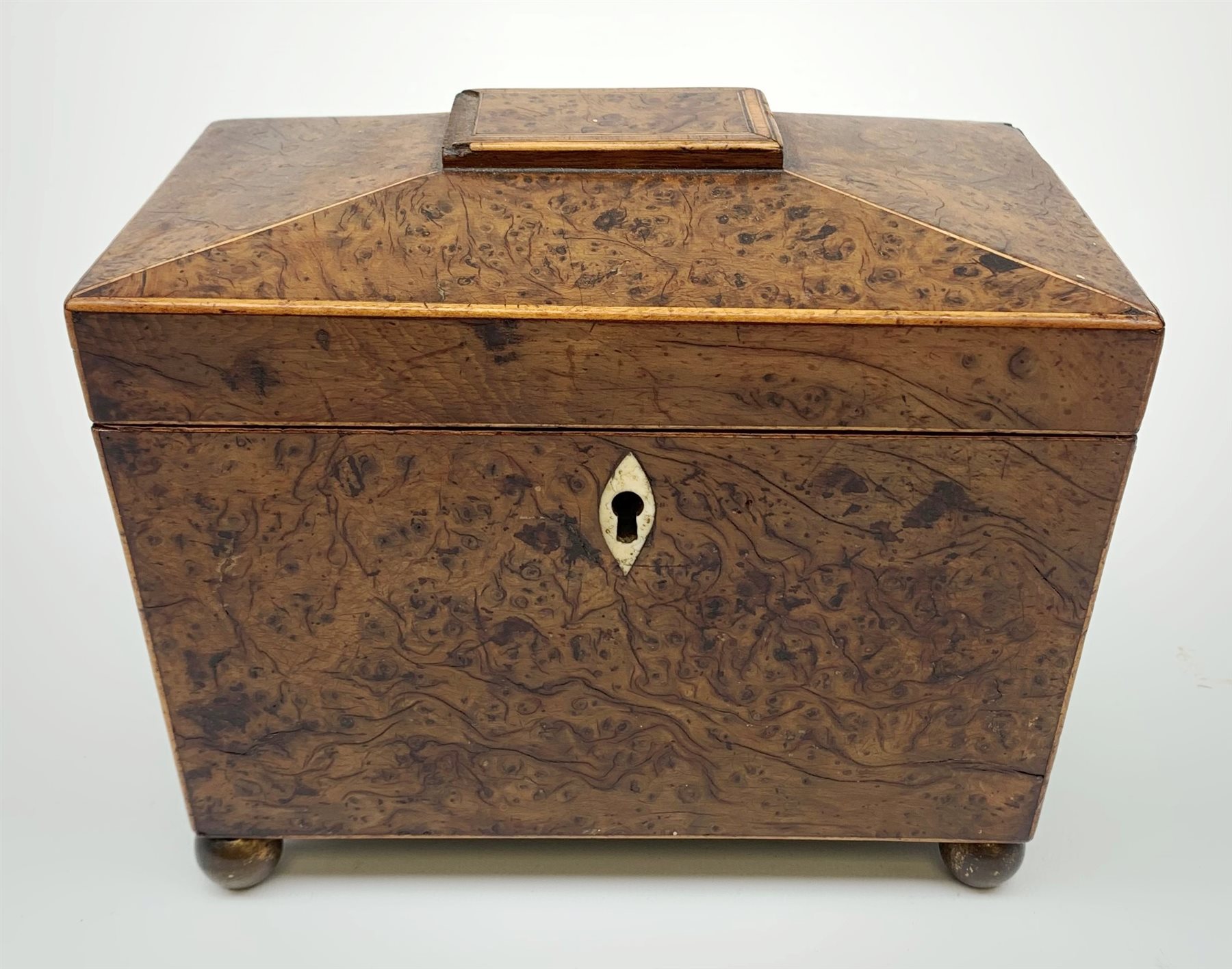 George III burr yew tea caddy, of sarcophagus form with lion mask ring handles and four brass ball feet, the hinged lid opening to reveal two compartments with cross-banded lids and traces of metallic paper lining, L19cm