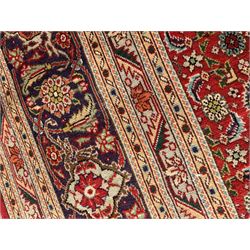 Large Persian Tabriz carpet, the red ground field decorated with repeating Herati motifs, multiple band border, the main band decorated with trailing foliage and flower head motifs