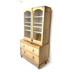 19th century stripped pine cabinet on chest, two glazed cupboard doors enclosing three adjustable shelves, two long drawers on the base unit, turned supports 