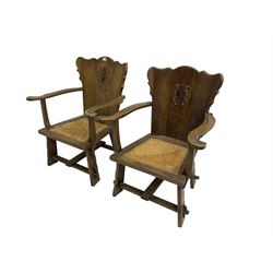 Pair Arts and Crafts oak armchairs, shaped cresting rail and back with carved and painted Heraldic crest, swept arms over drop-in rush seats, raised on shaped stile supports united by peg stretchers