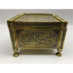Late 19th century Damascus Cairoware Quran box, of square form with canted hinged cover, upon four circular pad feet, the brass exterior inlaid with silver and copper script and decorative detail, opening to reveal a marquetry lined interior, H15.5cm W19cm D19cm