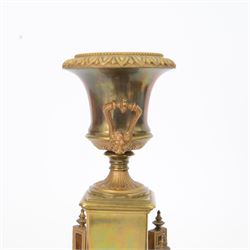 French- Art-deco Edwardian 8-day four-glass clock garniture, with etched glass panels, cast brass decoration to the corners of the case and splayed feet representing cloven hoofs to the base, case surmounted by a large oval urn on a tiered brass platform, two part dial with a recessed brass centre comprising of pierced radial decoration, with steel spade hands and Arabic numerals to the chapter, rack striking movement with a deadbeat Brocot escapement, striking the hours and half-hours on a bell. With a visible twin file mercury pendulum. Garni comprising two large twin handled urns on rectangular pedestals raised on conforming feet representing cloven hoofs, Clock and garni presented on three shaped wooden gesso bases with velvet pads. With key.