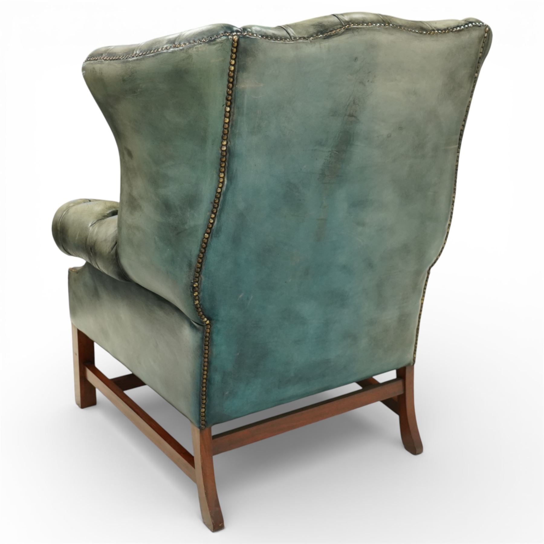 Georgian design mahogany framed wingback armchair, upholstered in rustic pale green buttoned leather with loose seat cushion, raised on square supports united by H-stretcher