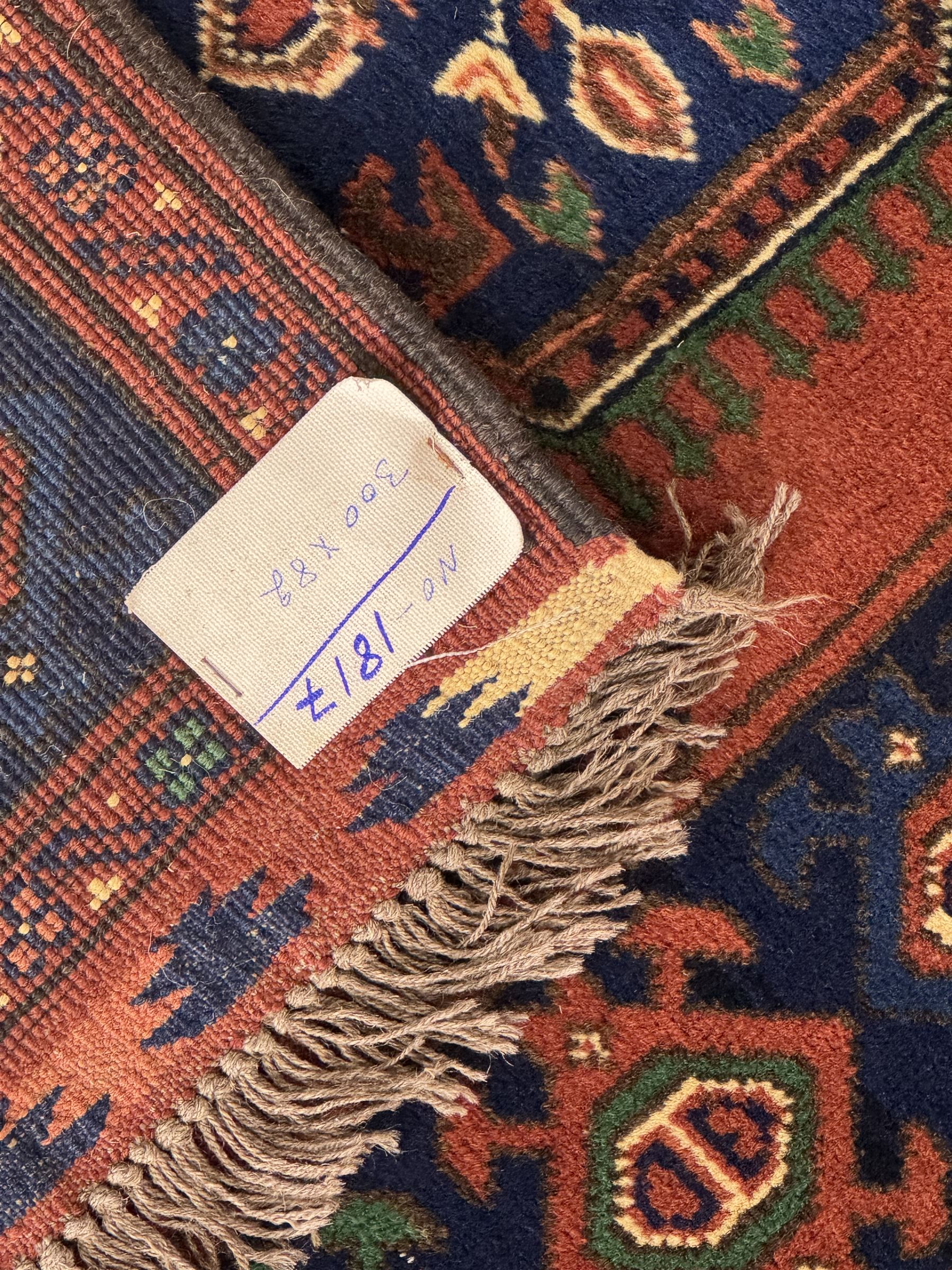 Late 20th century Afghan style ground runner, woven with a repeating panel design along a terracotta field and indigo grounds, framed by multiple narrow borders, and finished with fringed ends