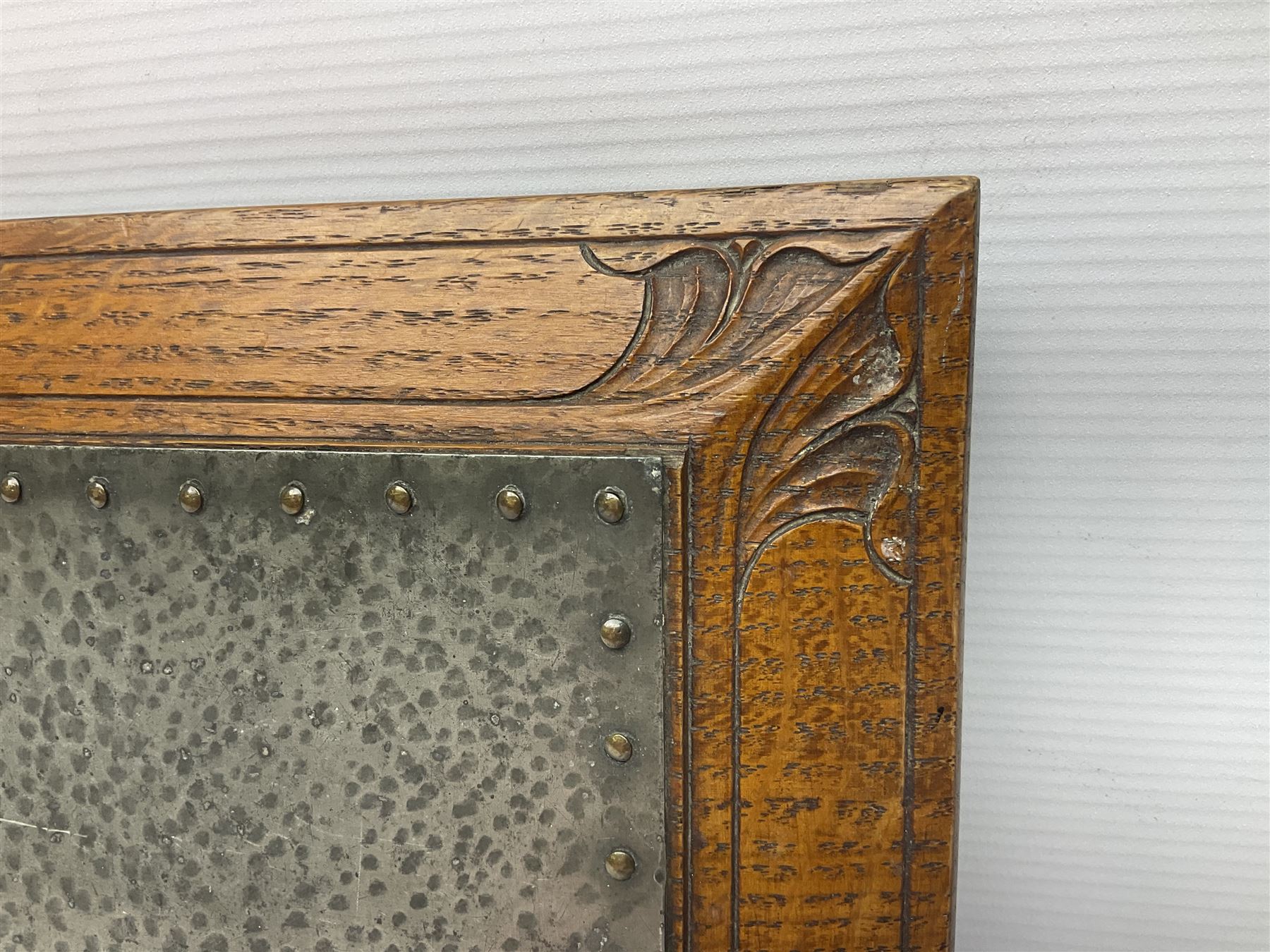 Arts and Crafts oak stand by Arthur Simpson of Kendal, of rectangular form with central hammered pewter panel, surrounded by a border with carved foliate corners, upon two bar supports, bearing label detailed 