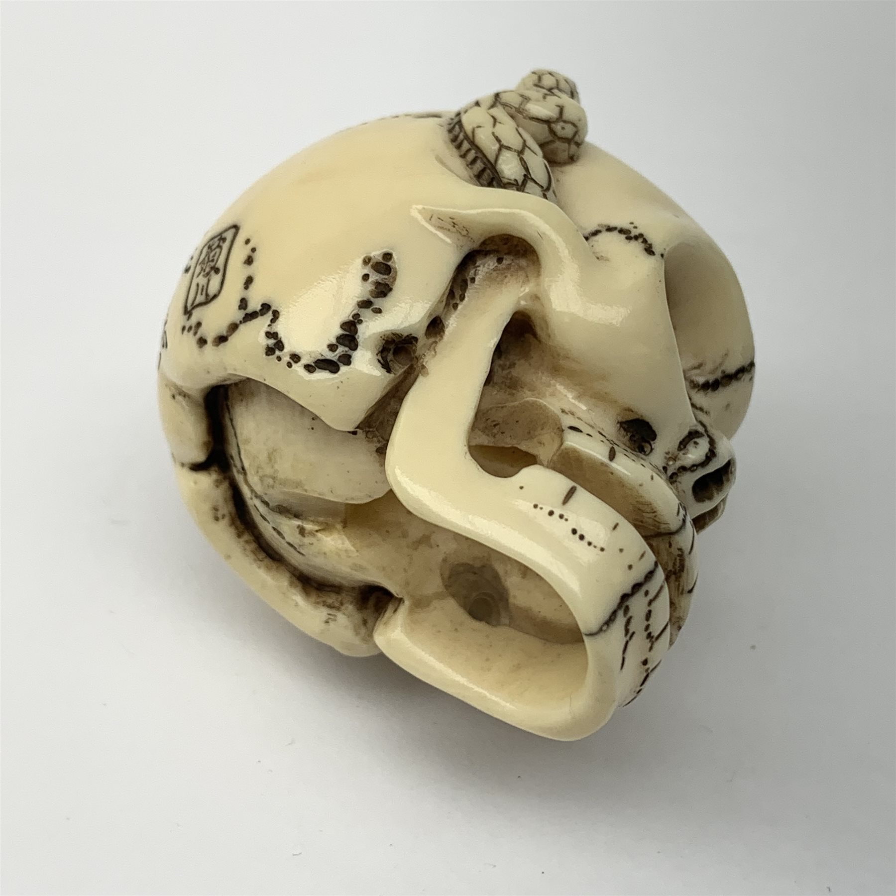 Japanese Meiji carved ivory netsuke, modelled as a skull, the top carved with two toads, and script and signature to reverse, L5cm, H4cm   