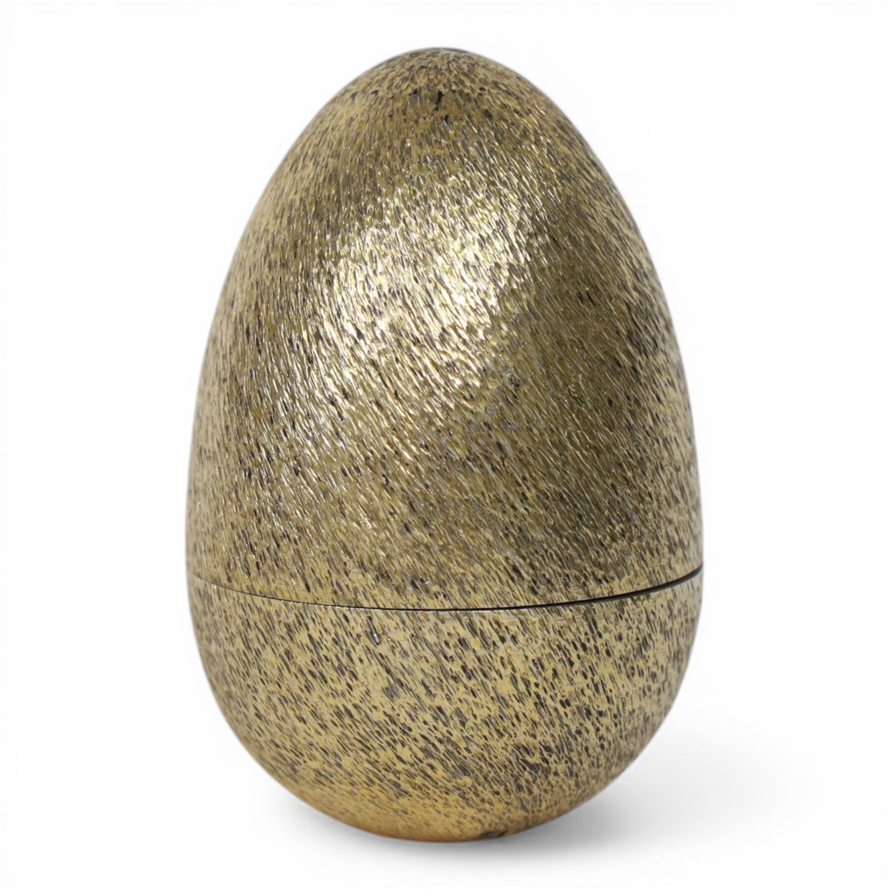 Late 20th century silver and silver-gilt surprise egg, the textured gilt exterior opening to reveal a clutch of chicks, the clustered heads supported upon a spring, within a jagged and lobed silver and gilt encasement, with green enamel surround, hallmarked Stuart Devlin, London 1982, H7cm