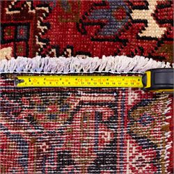 North West Persian Heriz hand-knotted carpet, madder red field, with a large central angular star medallion with stepped outlines on ivory ground, surrounded by geometric floral devices and stylized rosettes, with corresponding corner spandrels, enclosed by a bold geometric main border with multiple guard stripes, with cotton fringe ends 