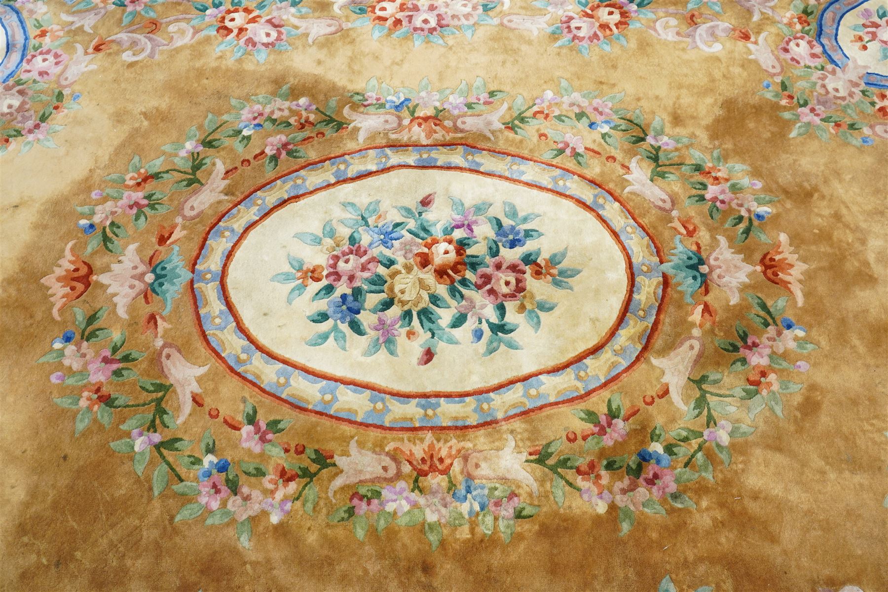 Chinese Aubusson/Savonnerie style hand-knotted carpet, ivory field with a central oval medallion issuing with stylized bouquets in shades of blush pink, pale blue, sage and green, enclosed by ribbon-tied floral garlands and conforming borders within narrow guard stripes, with cotton fringe ends 