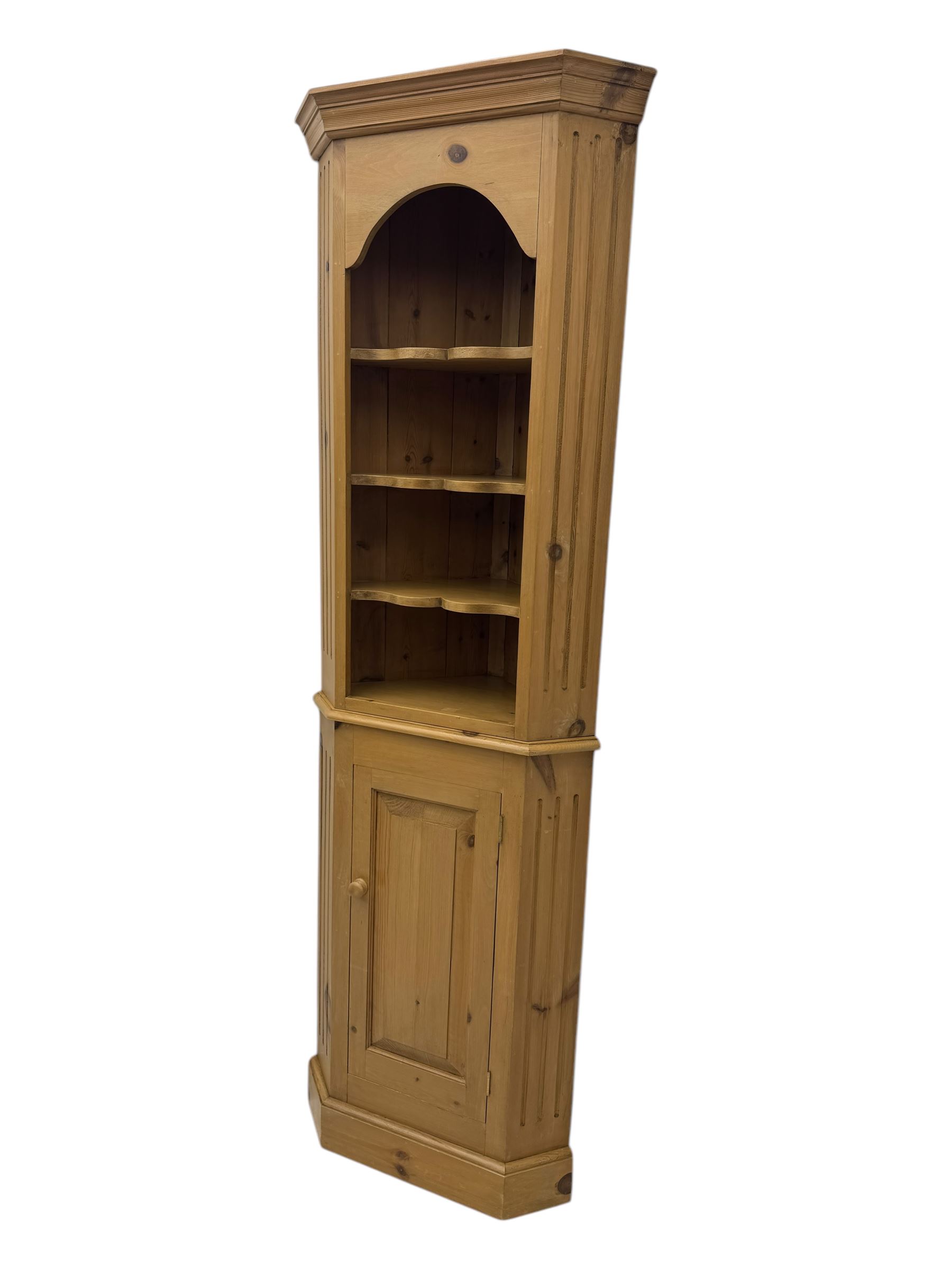 Early 20th century pine corner cabinet, projecting cornice over three shaped shelves, base fitted with single door enclosing storage space with a recessed panel, fluted sides, on plinth base