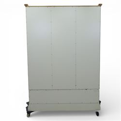 Modern triple wardrobe in white finish with oak moulded top enclosed by three doors with three drawers to base, with metal cup handles raised on bracket feet