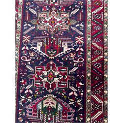 Northwestern Persian Heriz hand-knotted runner, dark indigo field with a series of linked stepped medallions in madder red, ivory, and green, flanked by angular floral motifs, within a madder red border of stylized rosettes and geometric vine motifs 405cm x 95cm