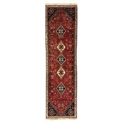 Persian Qashqai crimson ground runner, the field decorated with repeating diamond-shaped medallions flanked by angular floral motifs, the spandrels with intricate boteh designs, framed by an ivory border with stylised floral patterns and scrolling vines