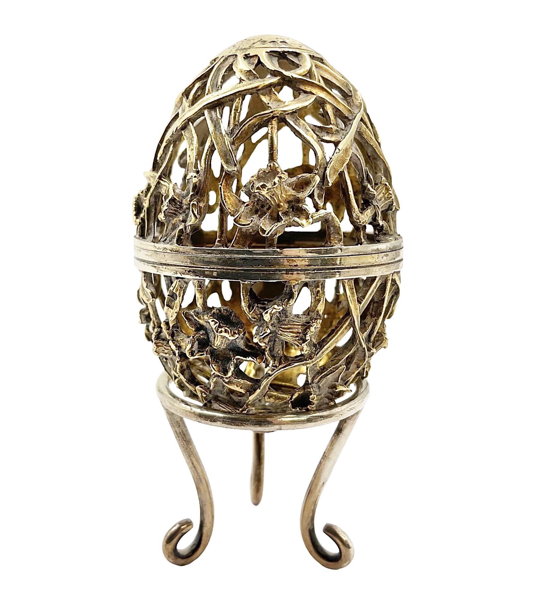 Modern silver limited edition Easter egg, no. 70/500, the gilt openwork body decorated with daffodils and detachable cover with pierced circular panel set with a single faceted blue stone, opening to reveal a gilt interior, upon silver stand with three scrolling pad feet, each hallmarked St James House Company, London 1980, height including stand 8cm