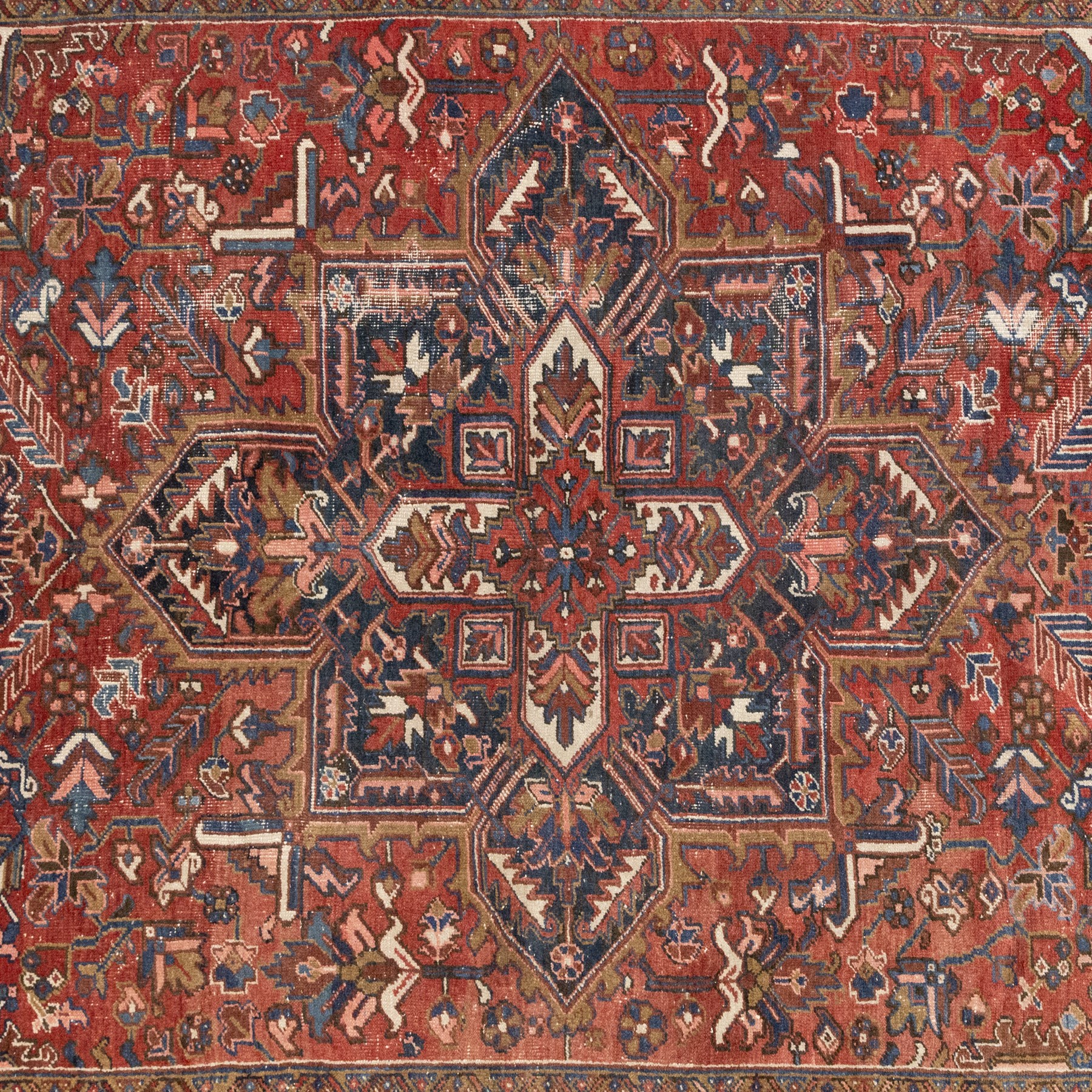 Persian Heriz carpet, red ground with large central geometric medallion, angular flowering branches and stylised foliate decoration, within a broad dark blue floral border and narrow guard stripes