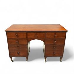 Early 19th century mahogany kneehole desk, rectangular moulded top over an arrangement of nine drawers with turned mahogany handles, arched kneehole recess, raised on short turned legs with brass cups and castors
