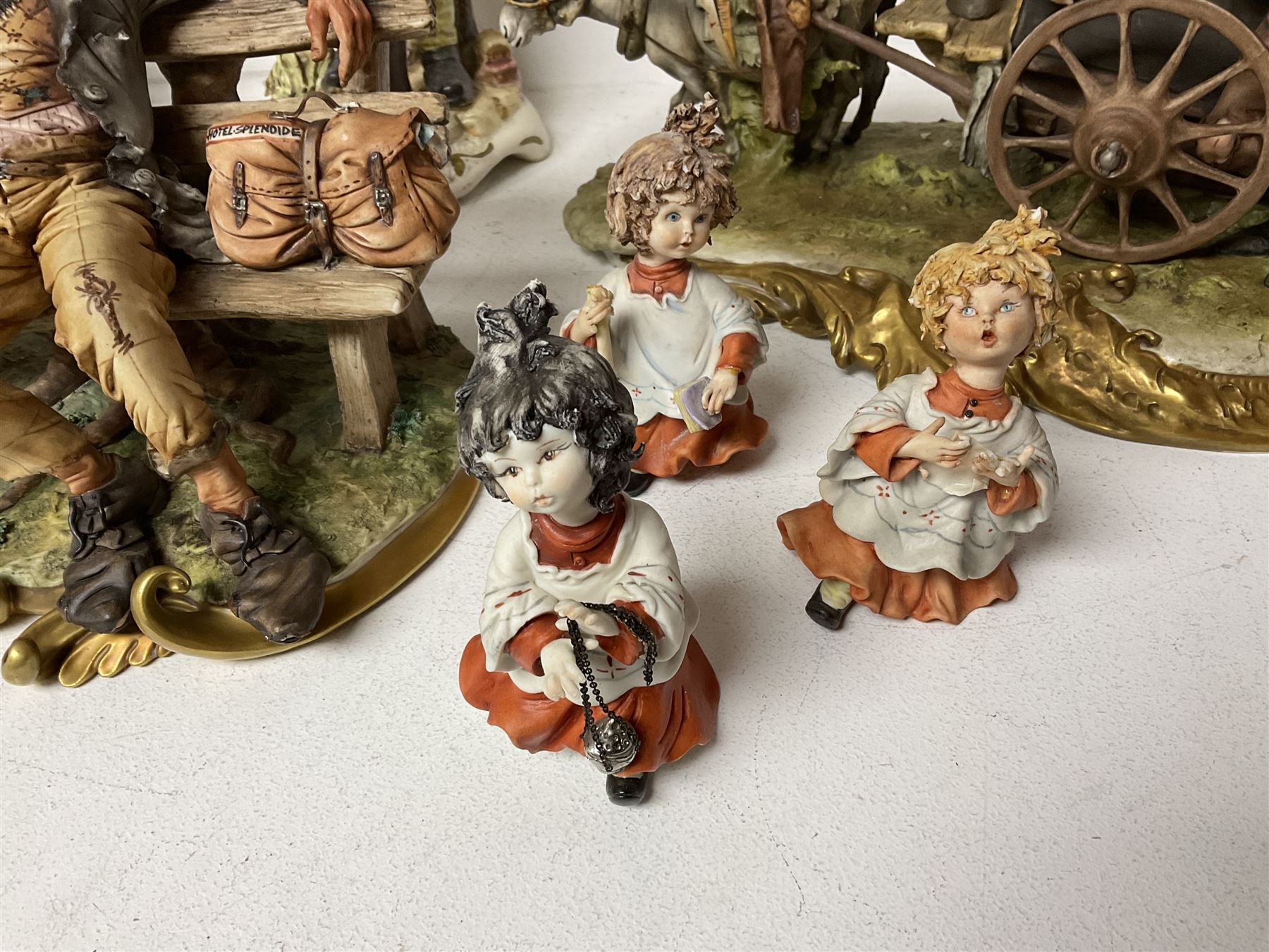 Group of Capodimonte figures, to include musical organ grinder with donkey and monkey, two tramp figures on benches, man with gun and choir boy and girl figures