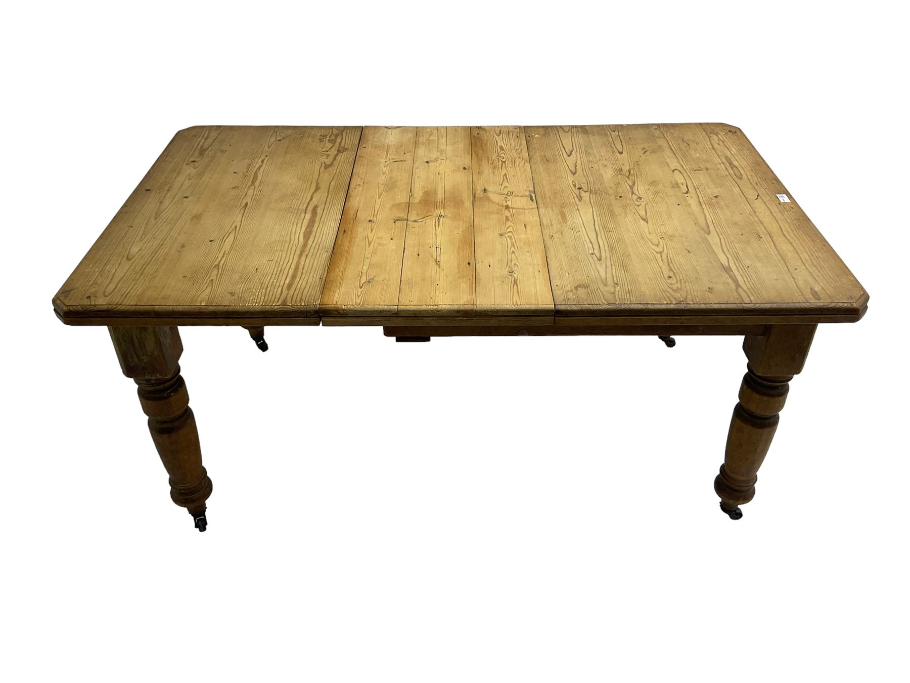 Late Victorian pine extending dining table, rectangular moulded top with canted corners and additional leaf, on turned supports with brass castors 