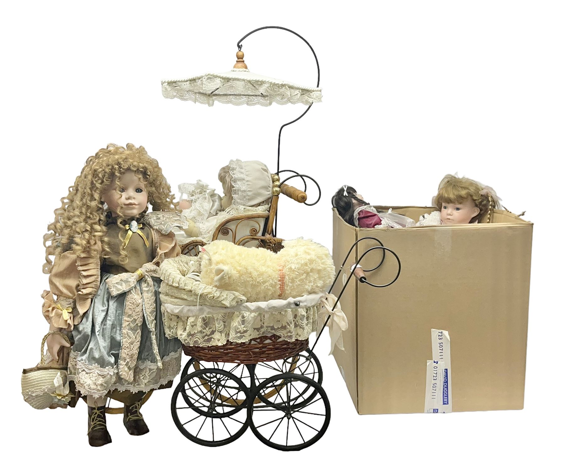 Two decorative wicker dolls prams, one with lace parasol,  and eleven dolls, including Leonardo Collection porcelain dolls, tallest pram including parasol H105cm