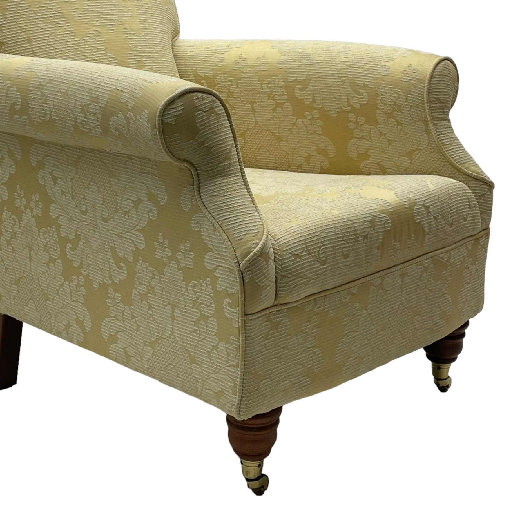Traditionally shaped hardwood-framed armchair, rolled back and arms, upholstered in pale gold and cream damask fabric with repeating foliate pattern, on turned feet with brass cups and castors