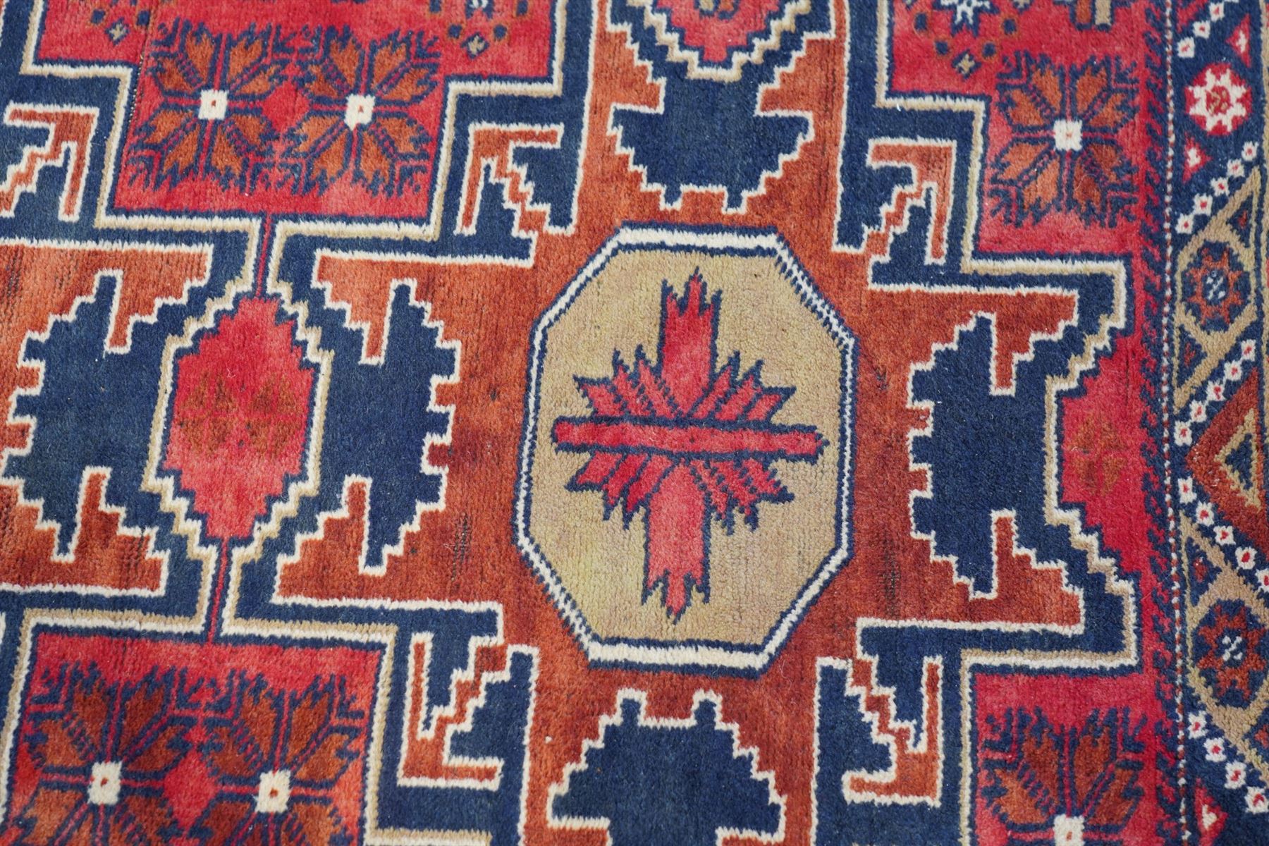Caucasian pale red ground rug, the field decorated with three large medallions and stylised flower heads, within repeating border 
