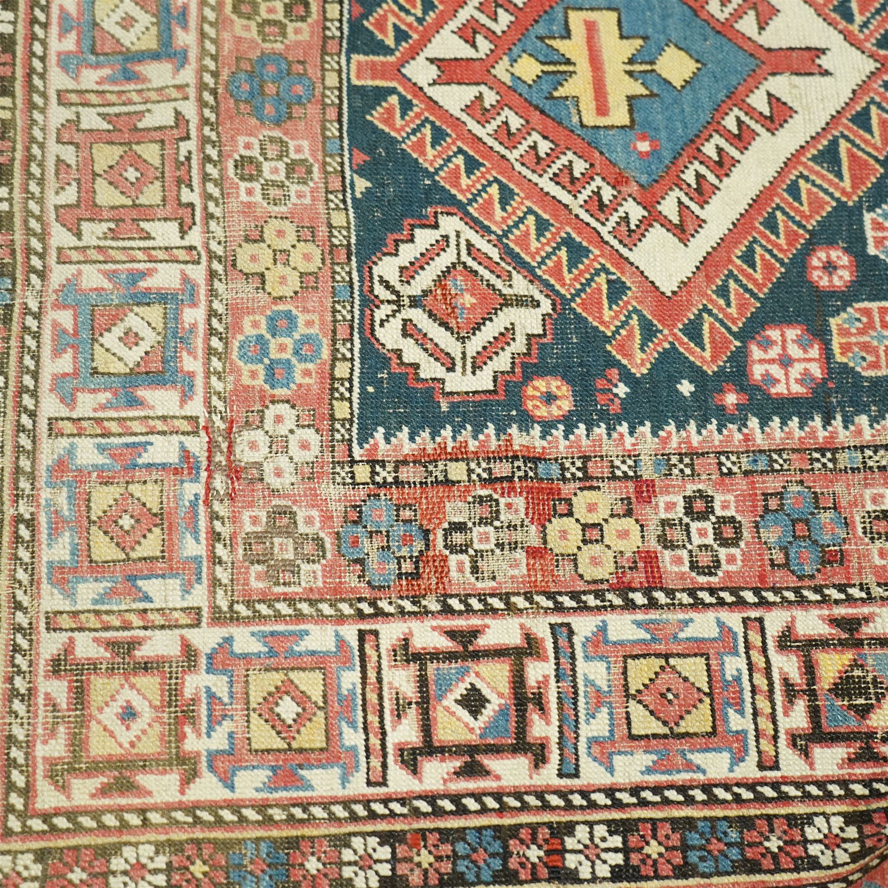 Vintage Caucasian Shirvan hand-knotted rug, indigo field with an arrangement of geometric diamond medallions and stylized tribal motifs within multiple patterned borders, with fringe ends 