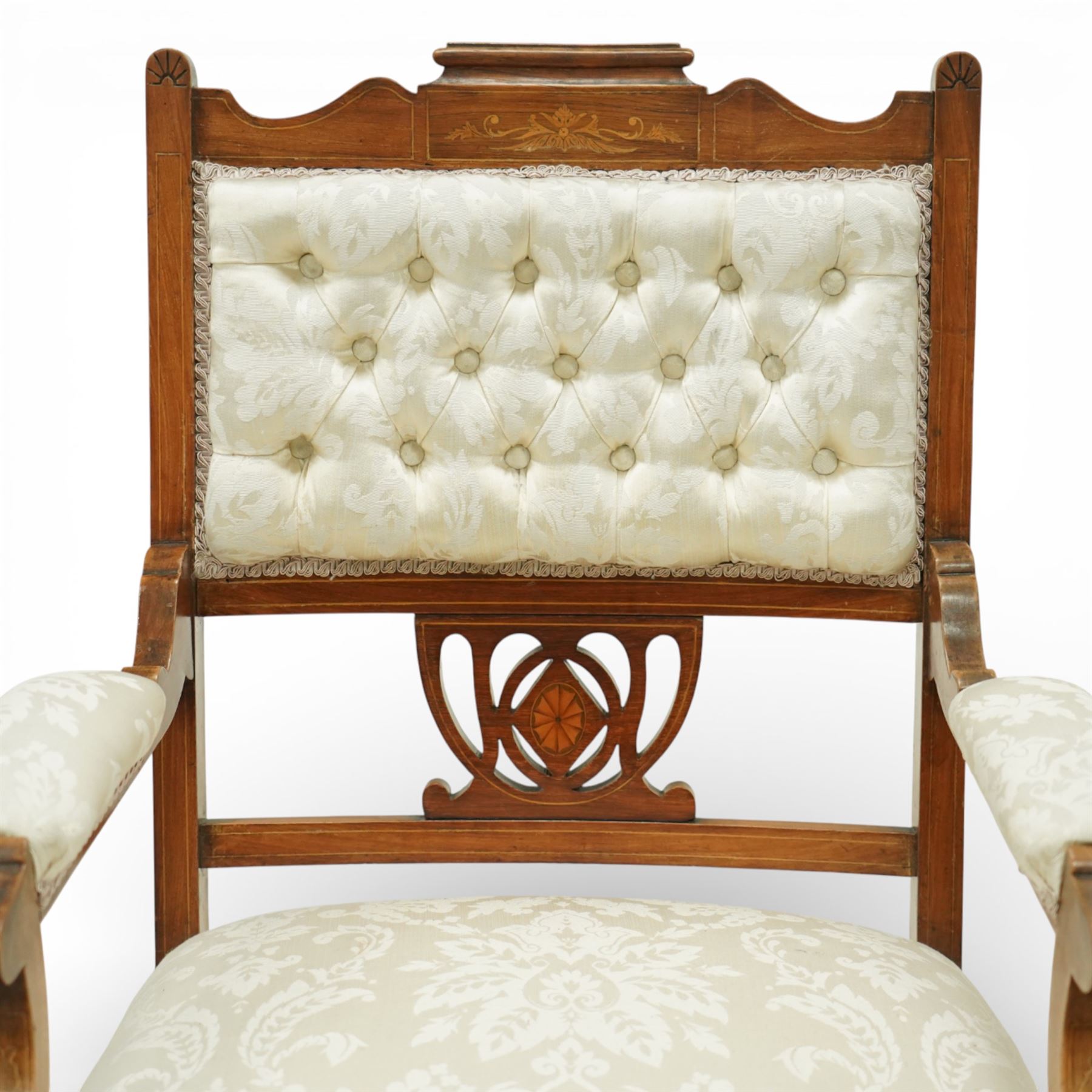 Edwardian mahogany open armchair, the upholstered rectangular back buttoned in ivory patterned fabric within a shaped top rail with inlaid foliate detail, open splat carved with a pierced anthemion motif centred by an inlaid roundel, swept open arms with upholstered pads, over a sprung upholstered seat, on turned front supports with brass castors