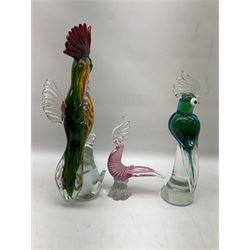 Three Murano style glass cockatoo parrots, the first with mottled yellow, red and orange body, clear outstretched wings, dark blue beak and red crest, raised upon clear stylised base, the second smaller parrot with merging blue and green body, and further with pink striped body, tallest H40cm
