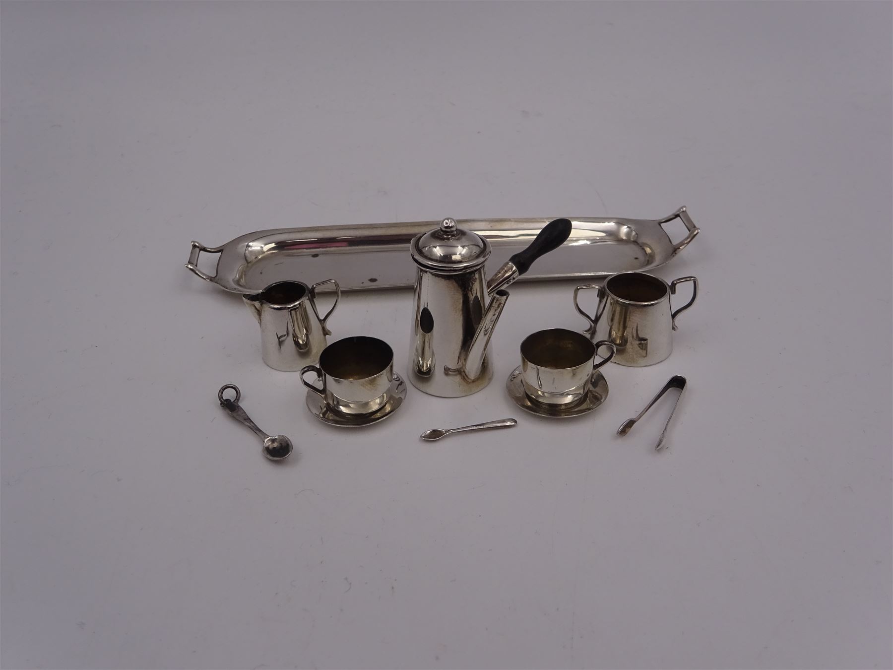 Edwardian miniature silver tea set, comprising hot chocolate pot, two cups and saucers, milk jug, sugar bowl and tray, hallmarked Cornelius Desormeaux Saunders & James Francis Hollings (Frank) Shepherd, Chester & Birmingham 1908, with two spoons and pair sugar tongs, hot water pot H3.8cm