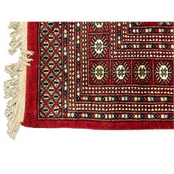 Pakistani Bokhara red ground rug, the field decorated with repeating Gul motifs and lozenges, the multi-band border with stylised plant motifs with dark indigo outlines