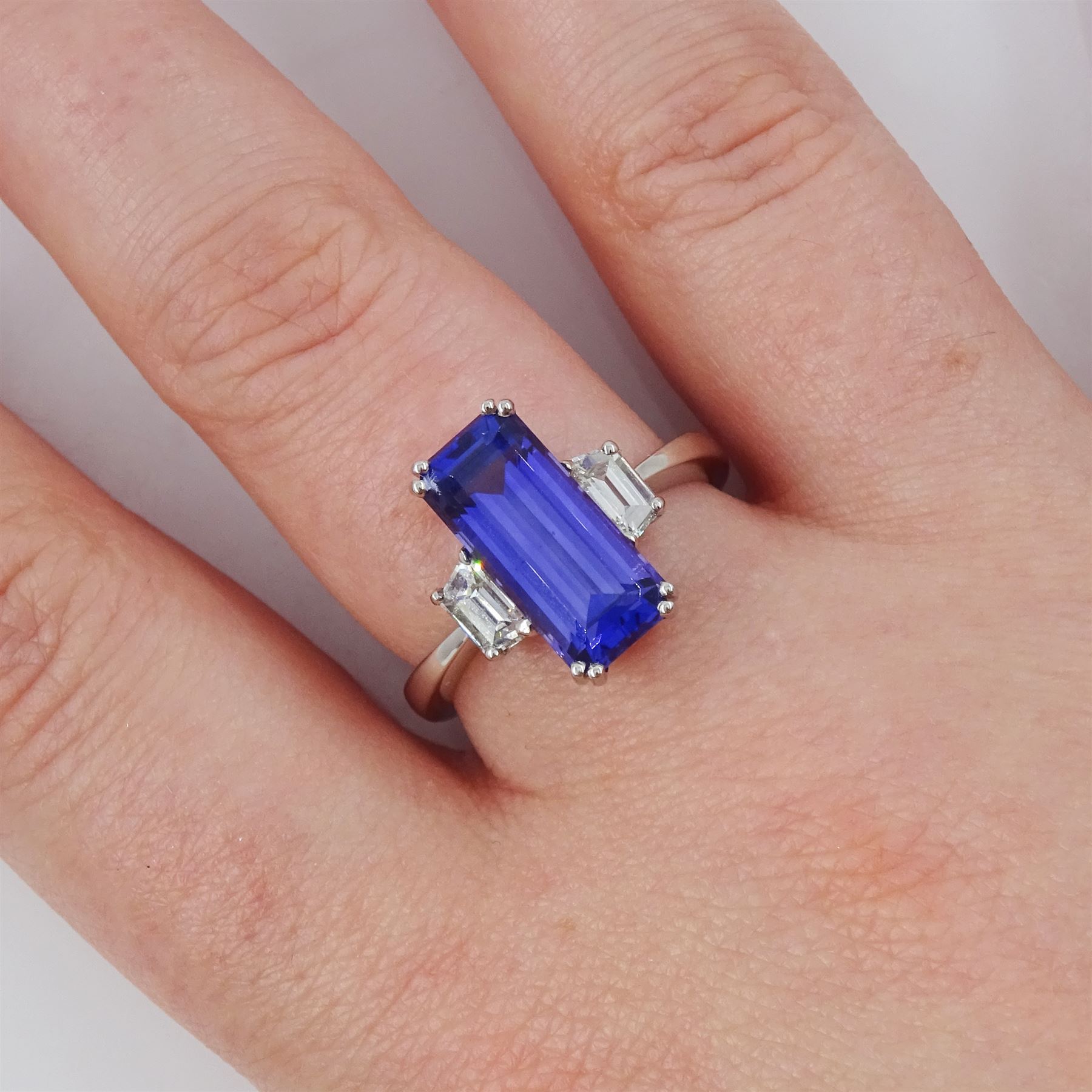 Platinum tanzanite and diamond three stone ring, single emerald cut tanzanite of approx 4.20 carat, with with a single trapeze cut diamond set either side, stamped PT950, total diamond weight approx 0.49 carat, with Alan Poultney Gems report