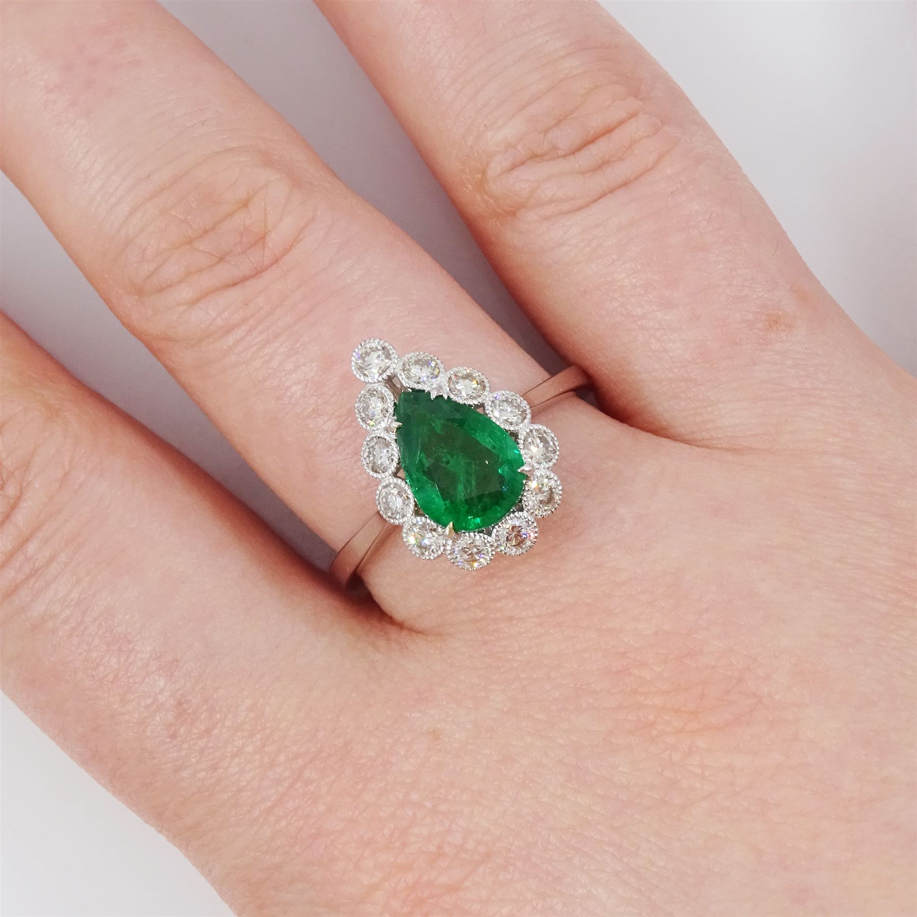 18ct white gold emerald and diamond cluster ring, single pear cut emerald of approx 1.40 carat, surrounded by twelve round brilliant cut diamonds, in a milgrain setting, stamped 750, total diamond weight approx 0.55 carat