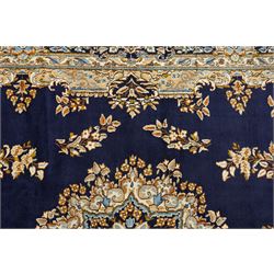 South East Persian Kirman hand-knotted carpet, indigo blue field with central floral medallion in tones of ivory, indigo,  and soft blue, issuing network of scrolling vinery, palmettes and floral sprays, conforming spandrels, broad main border of scrolling foliage and stylized palmettes, framed by multiple guard borders, with cotton fringe ends 