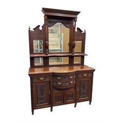 Edwardian walnut sideboard, projecting cornice supported by turned supports, the back fitted with three bevelled mirrors beneath fluted and flowerhead carved friezes, the lower section with four drawers and four panelled cupboard doors carved with foliate and urn designs, fluted uprights on turned feet