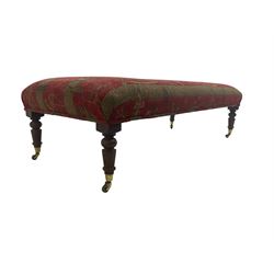 Large rectangular footstool, upholstered red and gold fabric decorated with Egyptian motifs, on turned supports with brass cups and castors; together with two matching scatter cushions 