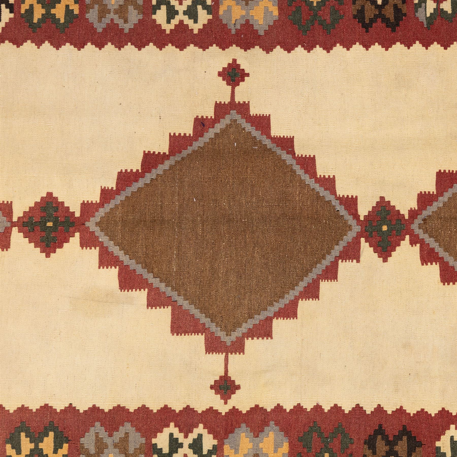 South West Persian Qashqai kilim, woven in flatweave in earthy tones, camel brown, ivory, olive, green, black, and madder red with three bold lozenge-shaped medallions, geometric borders incorporating stepped, hooked, and rosette motifs 