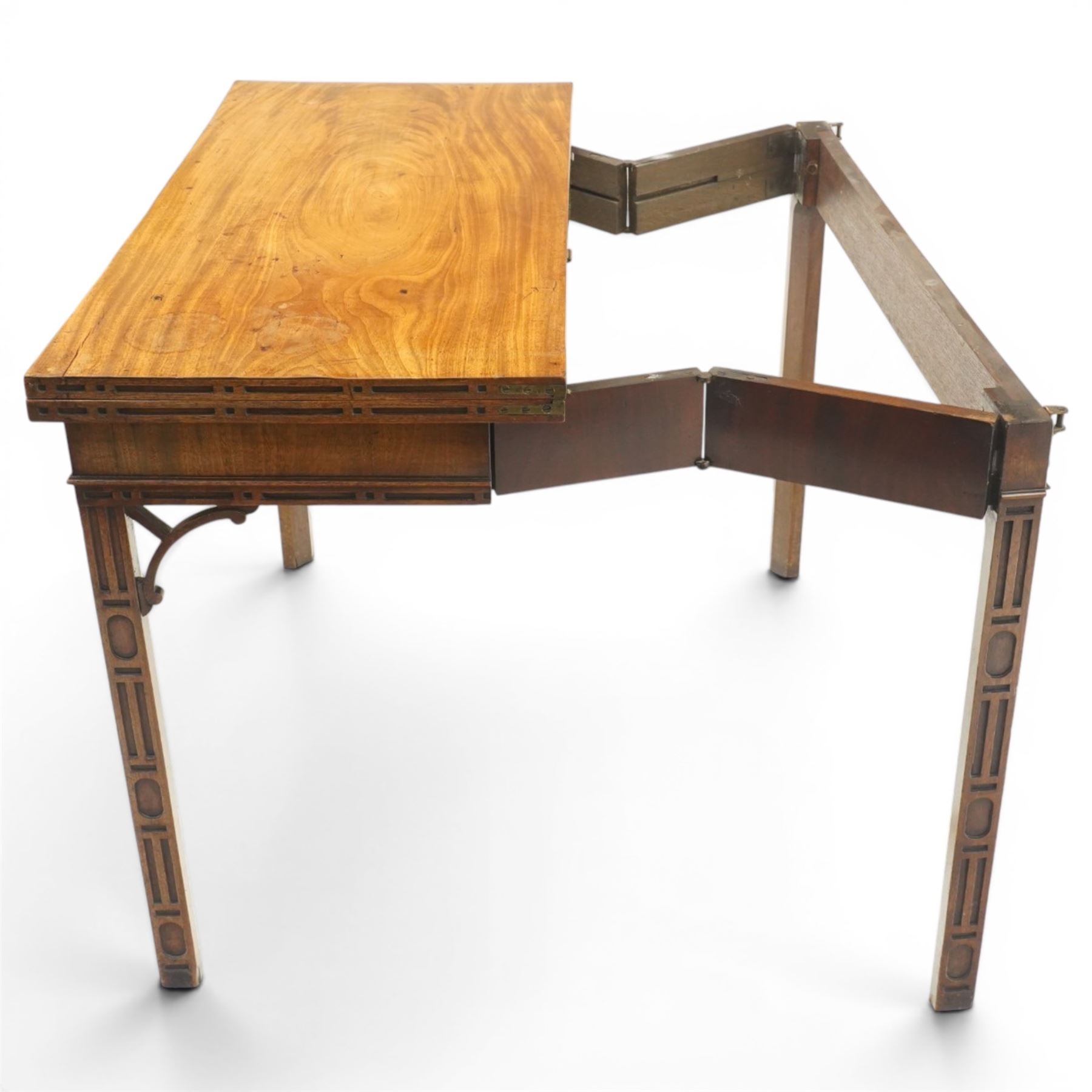 George III Chippendale design mahogany table, the rectangular hinged top with geometric carved edge, opening to reveal a baize-lined interior supported by twin concertina rear gateleg supports, over a banded frieze and pierced C-scroll spandrels, the inner chamfered square supports carved with geometric blind-fretwork detail