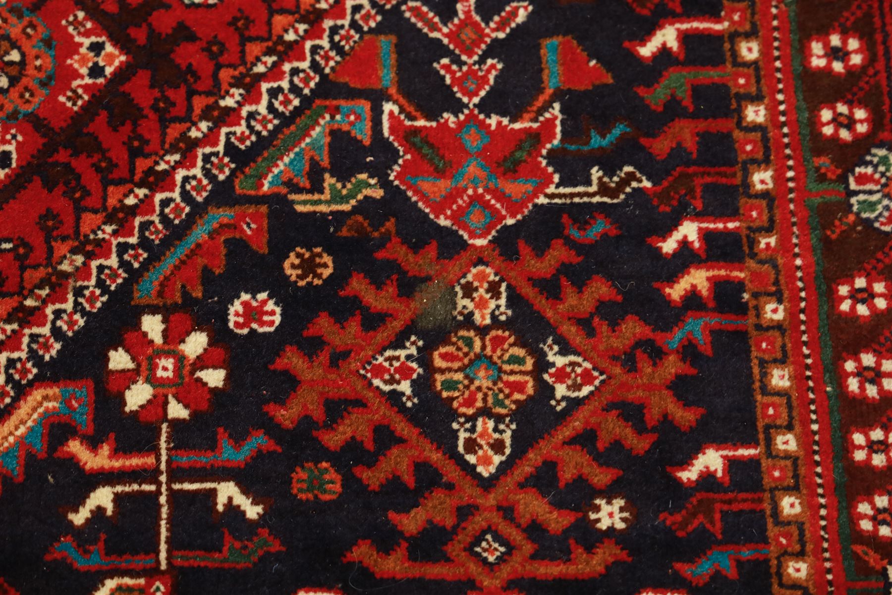 Persian tribal hand-knotted rug, crimson ground, madder field with central stepped lozenge medallion with scattered floral and geometric spandrels with rosette border 