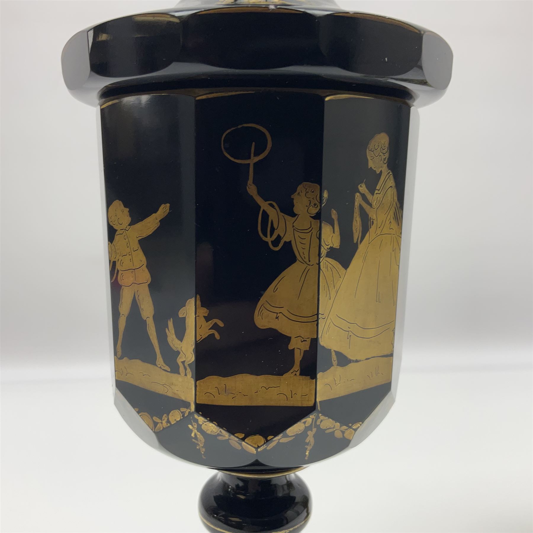 19th Century Bohemian amethyst glass lidded goblet, the bowl of faceted form, gilded with three children in period dress playing games, upon a knopped stem and conforming faceted foot, together with an art nouveau green glass goblet, with gilded rim, upon clear trumpet stem, and a hand blown wine glass, transfer printed with birds and three figures in period dress, tallest H29cm