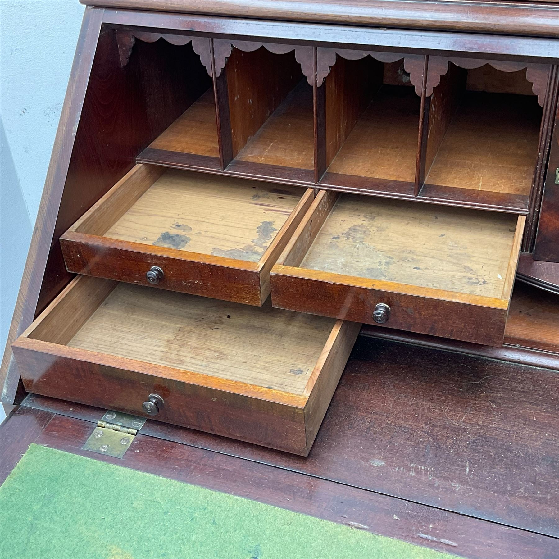 Early 19th century figured mahogany bureau bookcase, projecting splay moulded cornice over three adjustable shelves enclosed by two glazed doors, fall front revealing pigeonholes, cupboard and drawers, pull-out strays with scroll carved terminals, double cupboard with two panelled doors, on turned feet 