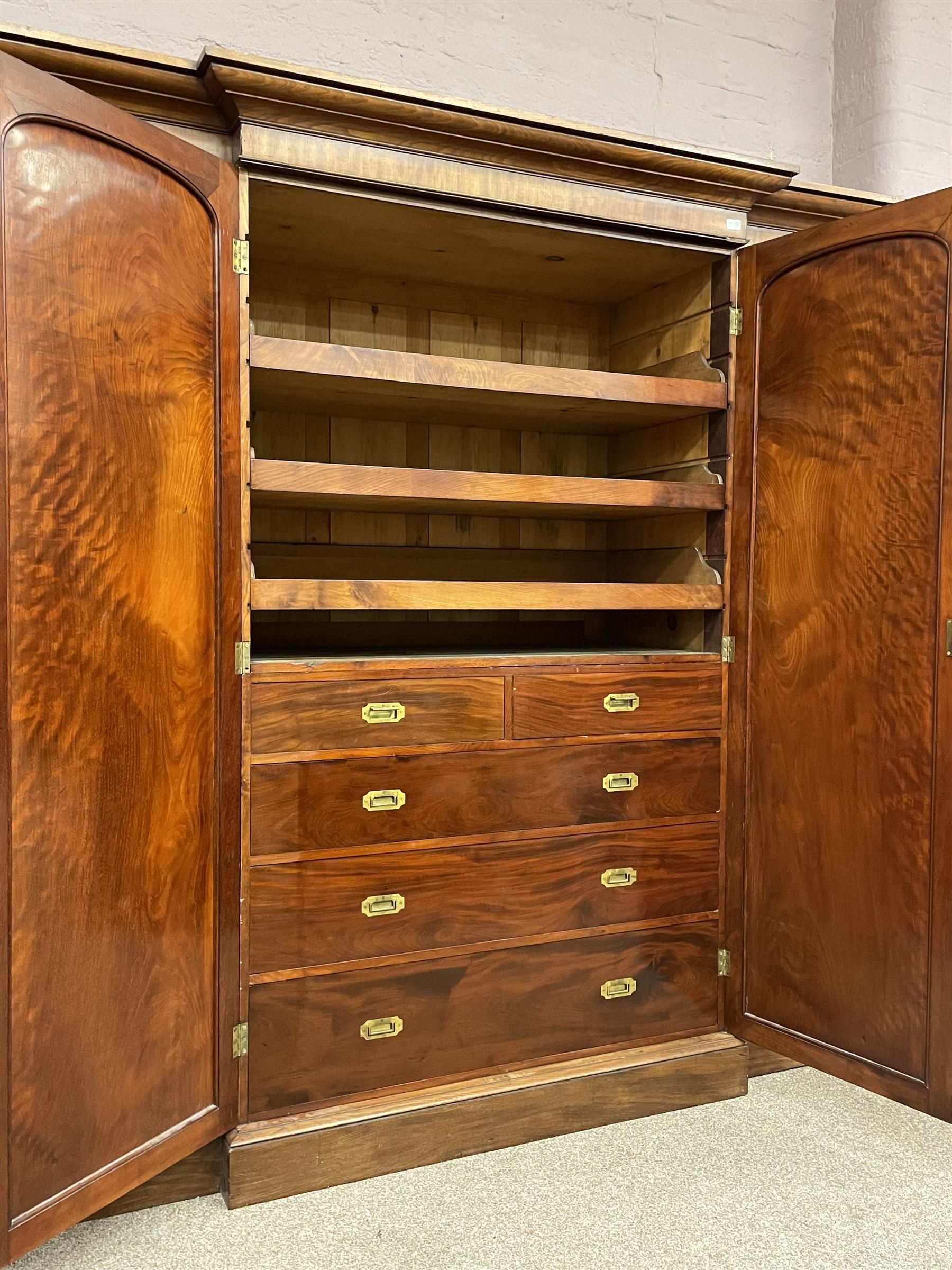 19th century figured mahogany quadruple breakfront press wardrobe, projecting cornice with banded frieze over arch panelled doors, the interior fitted with three sliding trays over two short and three long graduating drawers with recessed brass handles, flanked by two hanging cupboards with hooks