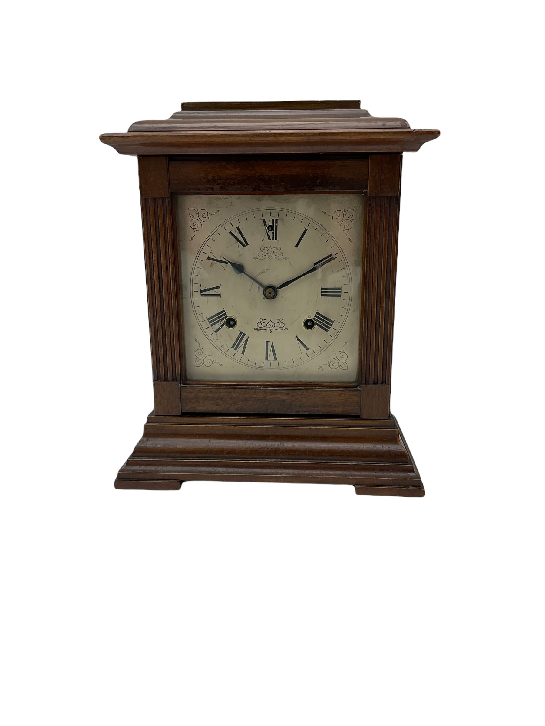 An American Mantle clock in a mahogany case with an eight-day “Ansonia” striking movement, case with a flat top and reeded pillars on a broad plinth with raised feet, square engraved and silvered dial with roman numerals and minute track, steel spade hands and pendulum regulation, sounding the hours and half hours on a coiled gong. With pendulum and key.  





